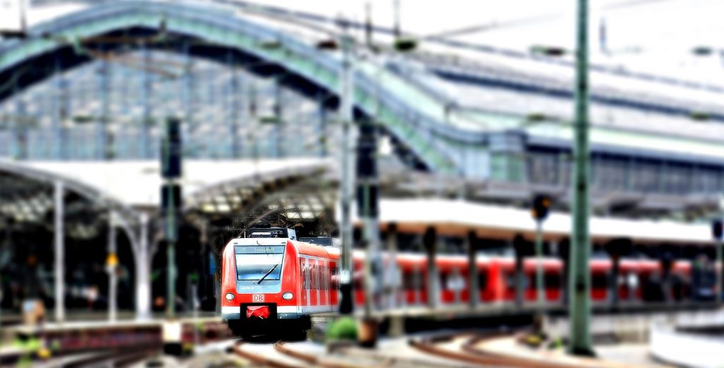 red train on tracks leaving a train station